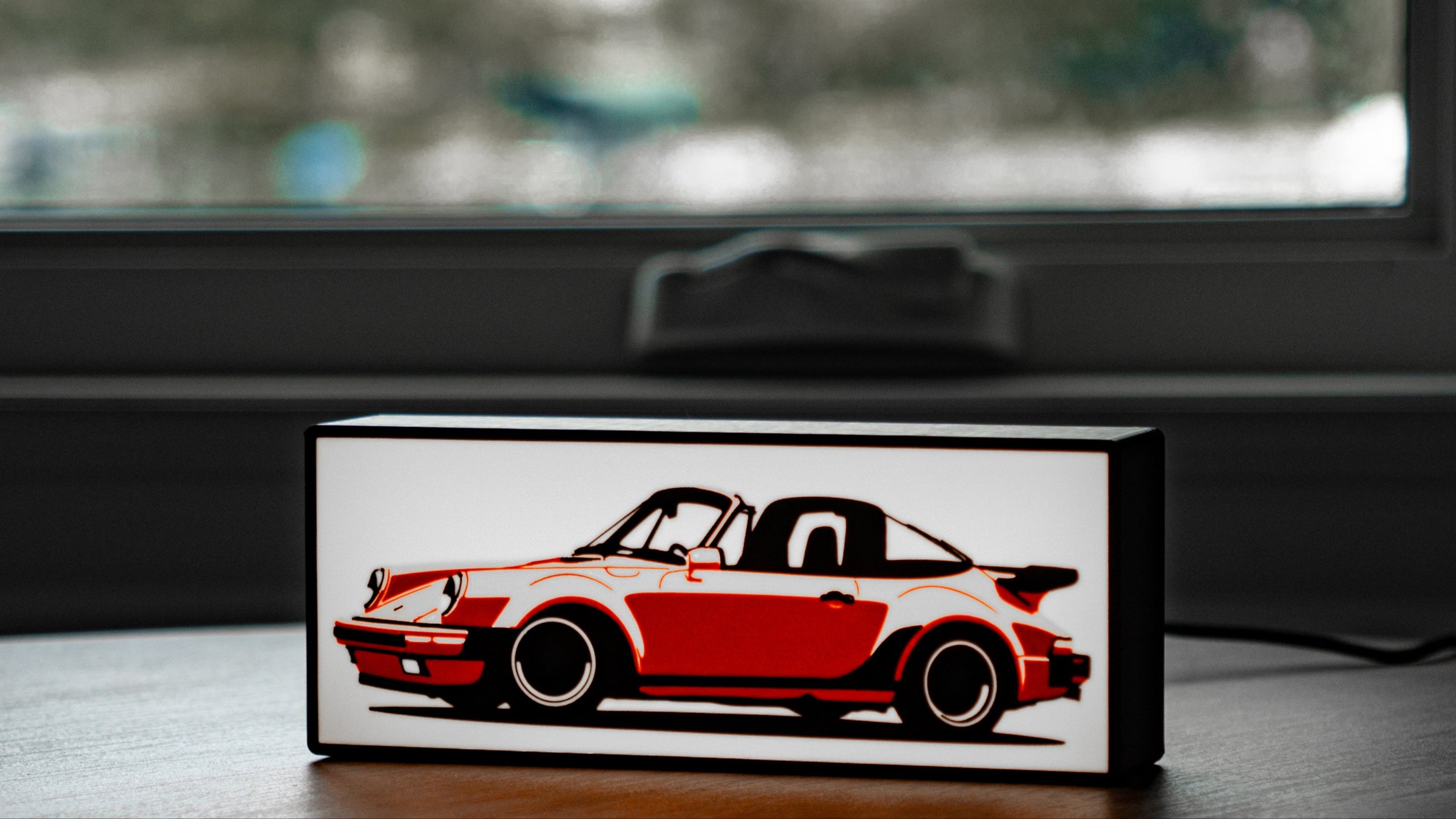 Small rectangular light box with a red and black car design on a wooden surface.