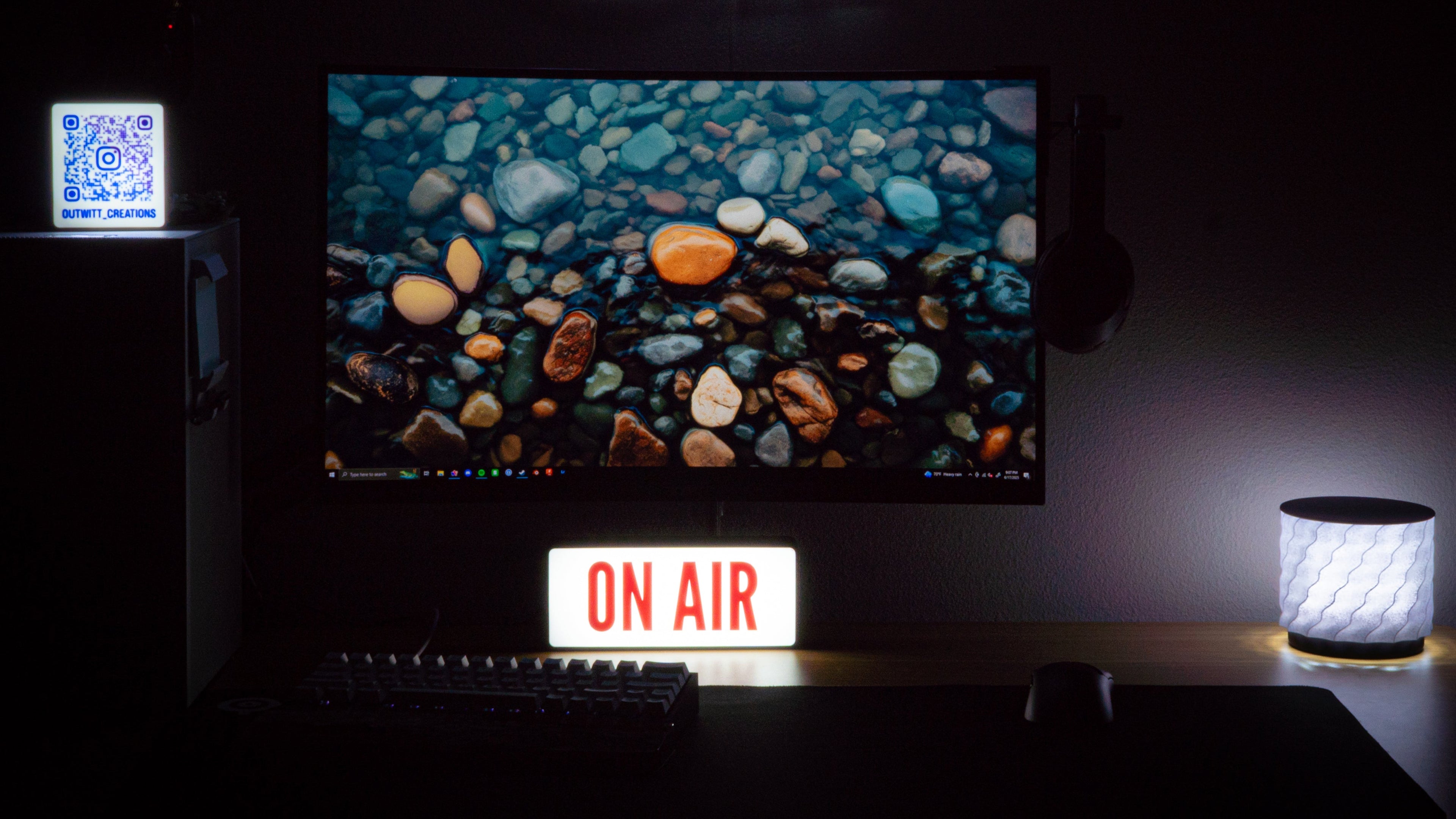 Dark room with computer setup, monitor displaying nature scene, 'ON AIR' sign, and glowing 'OW' logo.